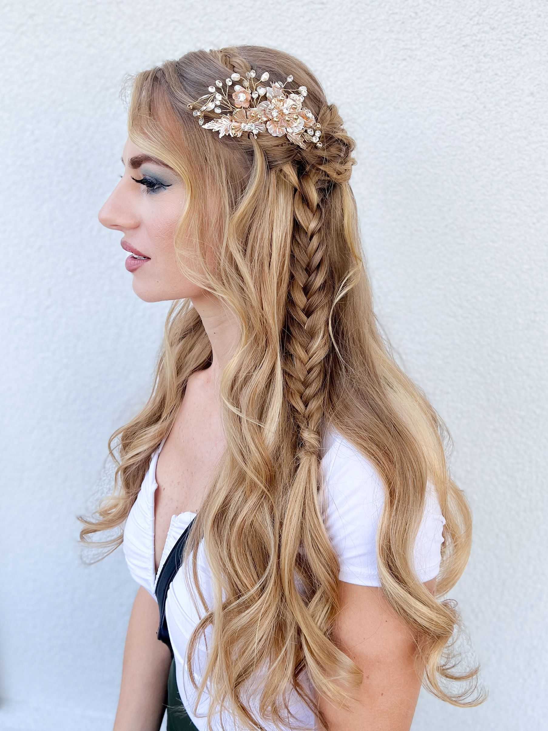 Woman with long braided hair and floral hairpiece against a white background, wearing a white top.