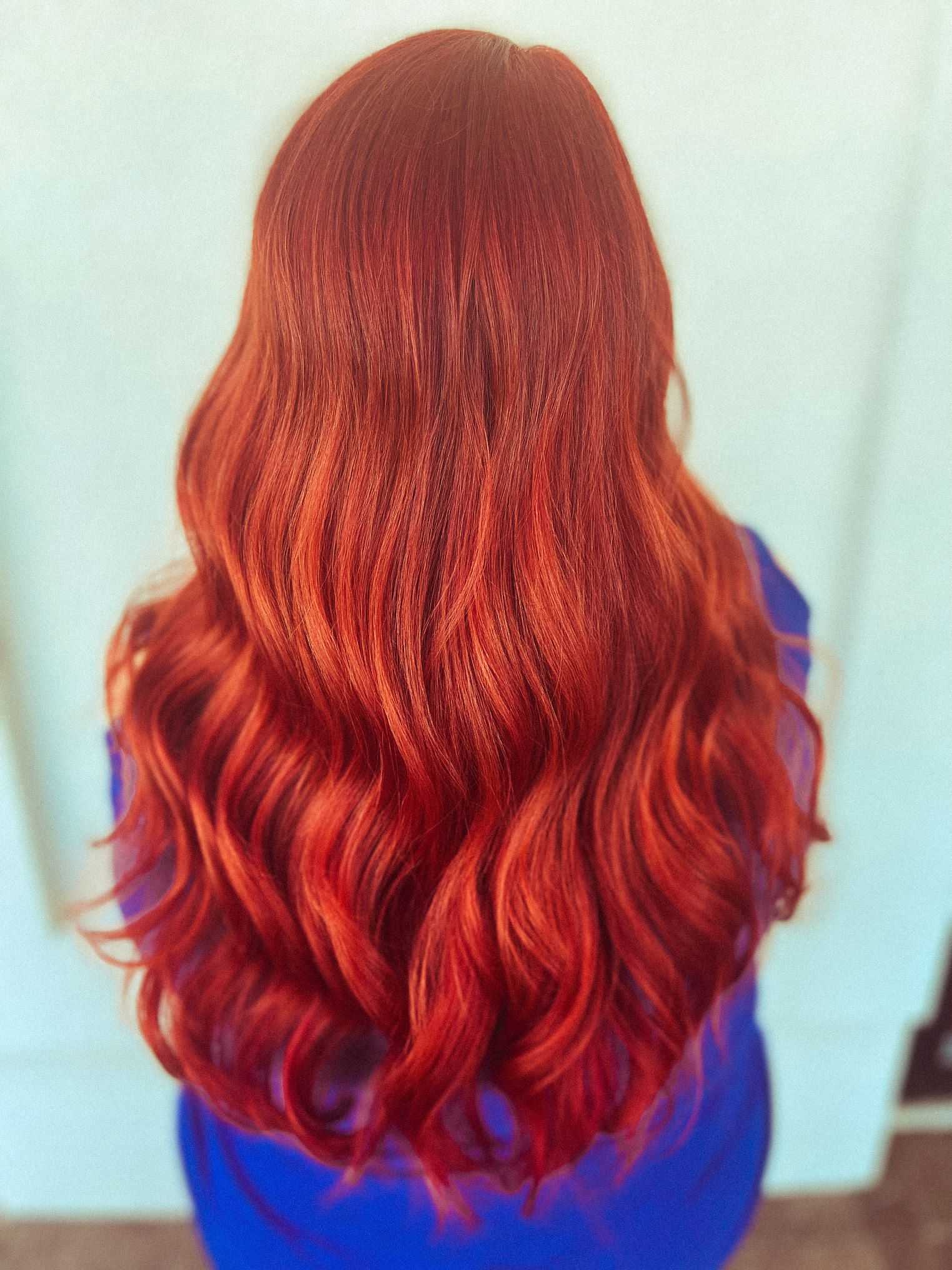 Woman with long, wavy red hair seen from the back, against a white background.